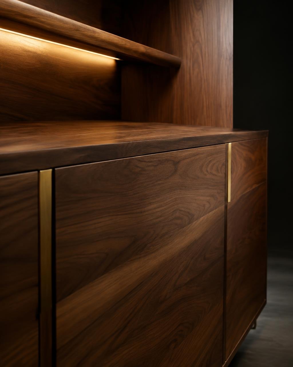 Close view of oiled walnut cabinetry with an integrated brass pull and warm under-shelf light