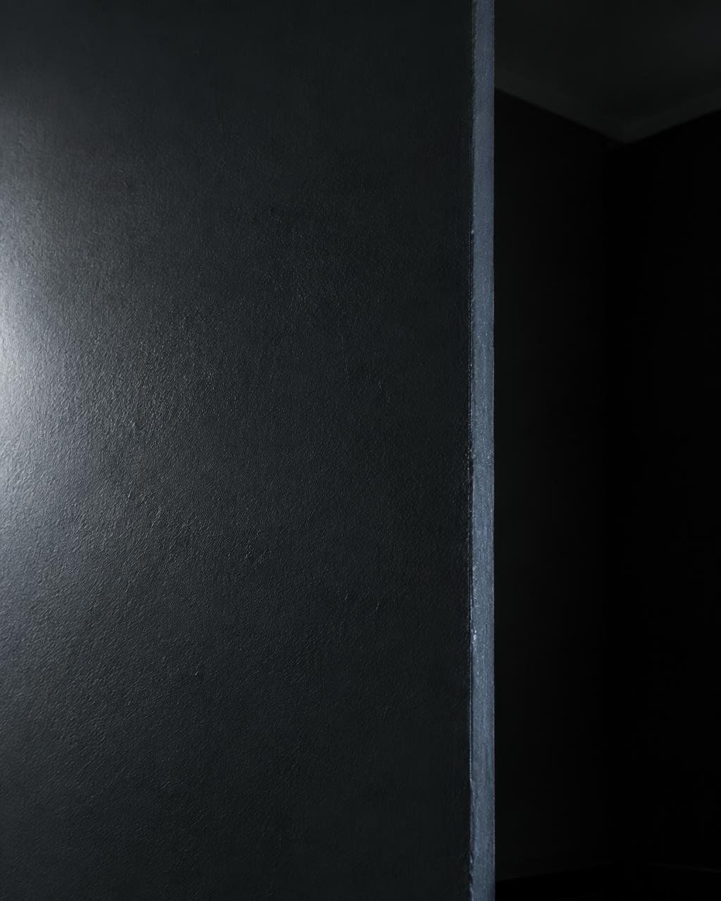 Freshly painted deep charcoal wall meeting a crisp reveal edge under raking light